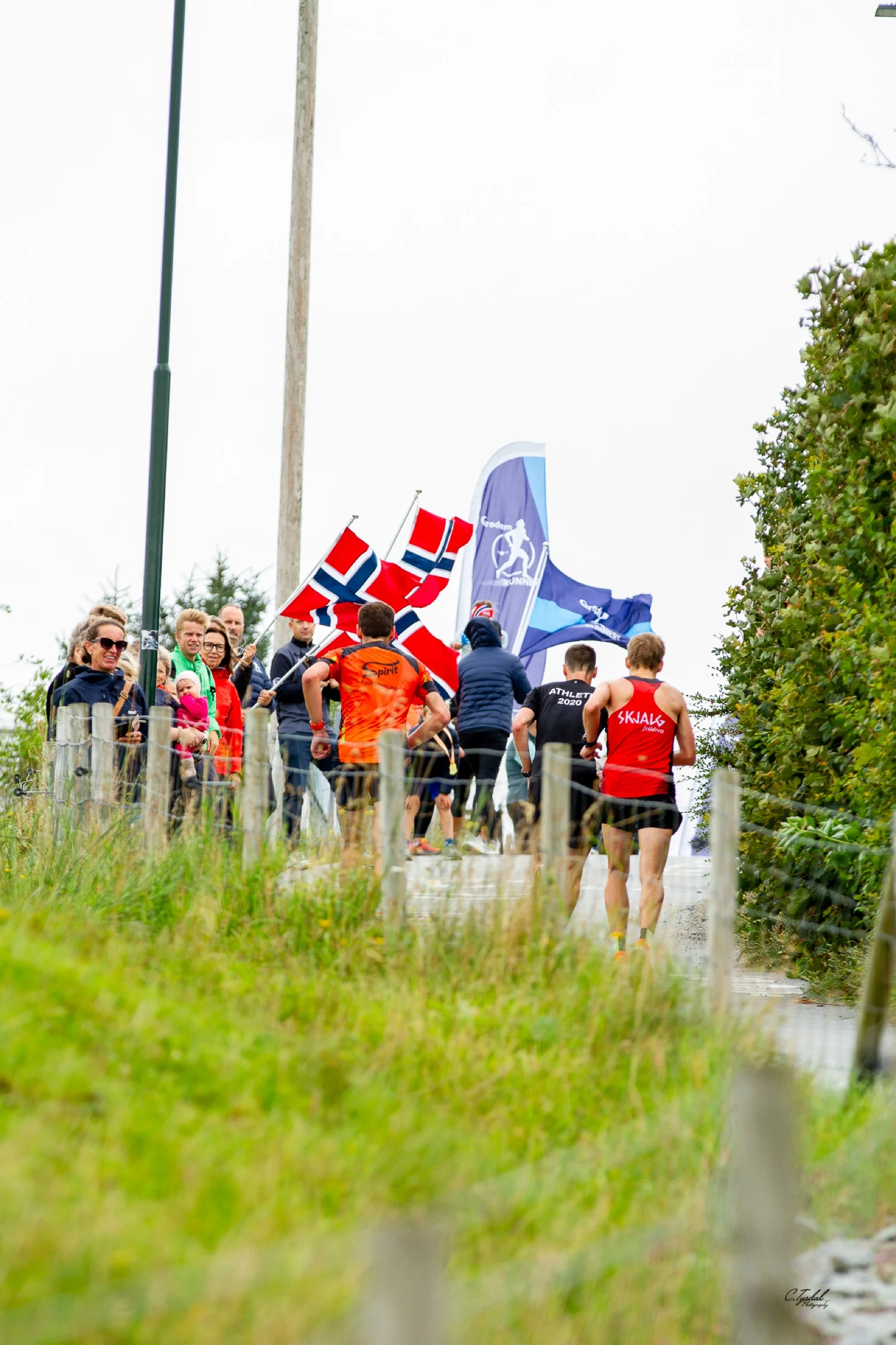 Løpere møter publikum og flagg i bakken under Lavterskel-løpet 2025